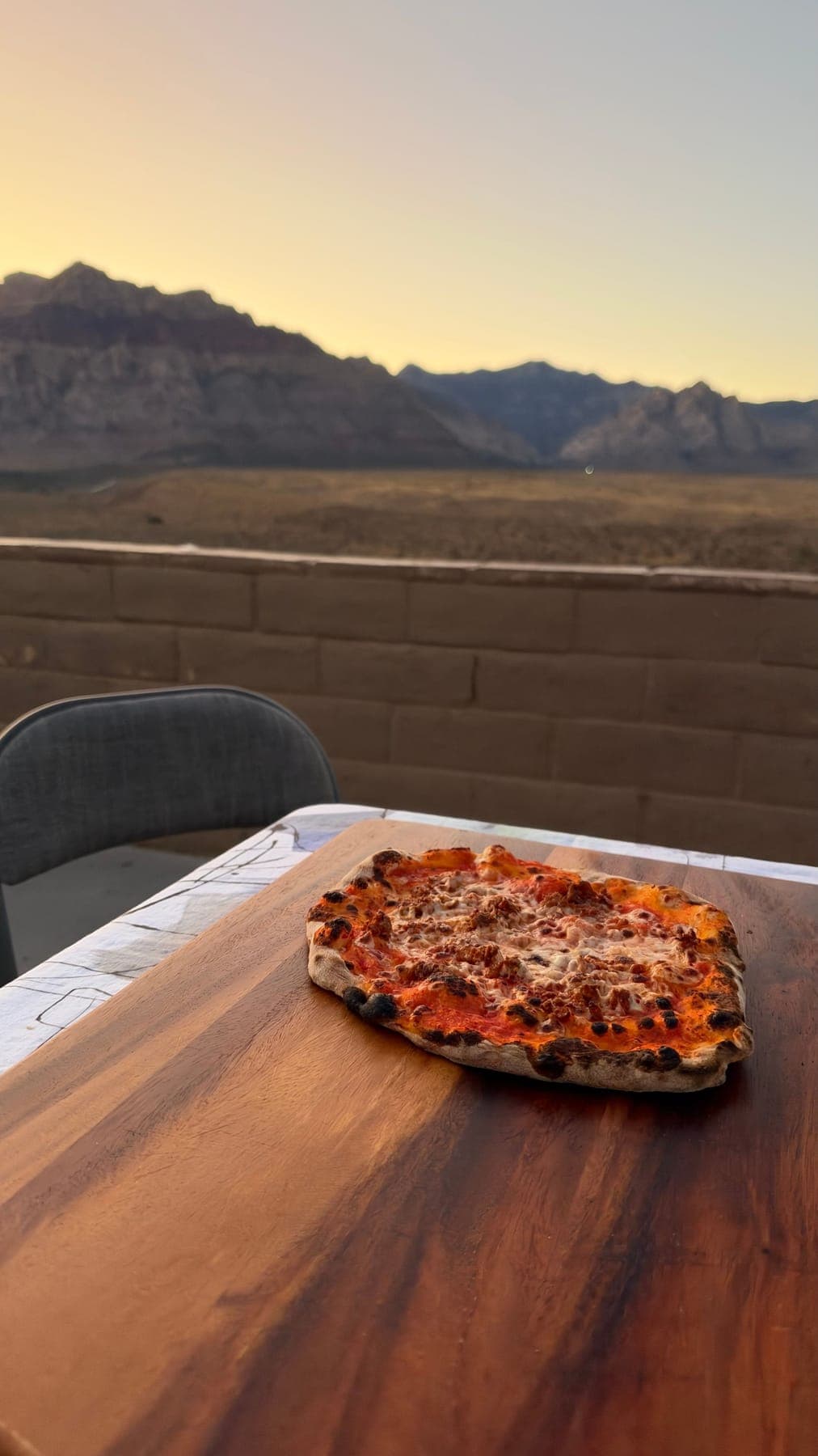A wood-fired pizza on a board at sunset, Red Rock mountains behind